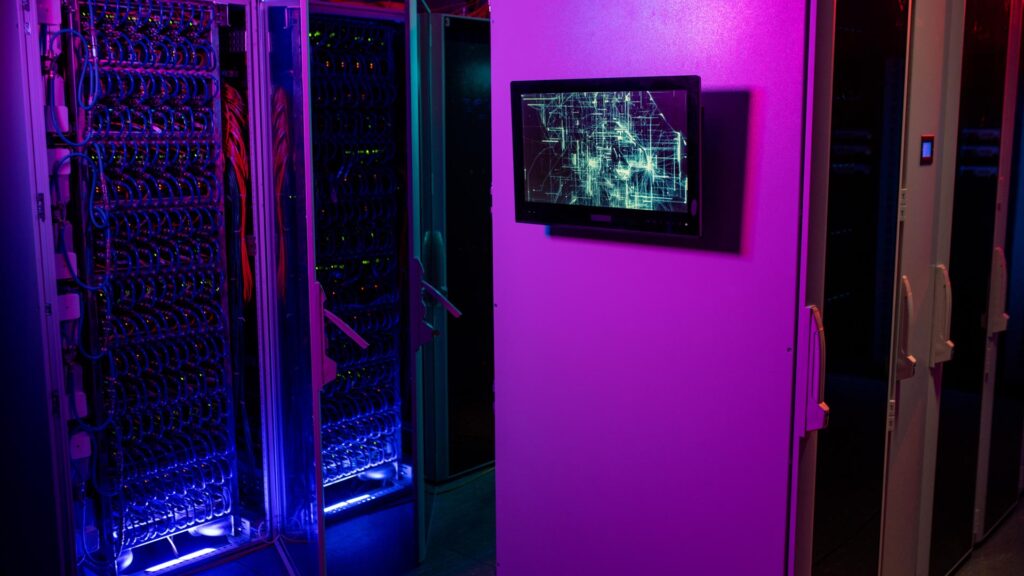 Monitor hanging on server rack cabinet in data center in neon purple and blue colors, open cabinet with blue cables in background